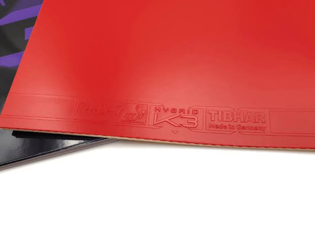 A close-up of a red table tennis rubber sheet with embossed branding reading 'TIBHAR HYBRID K3' on a white background.